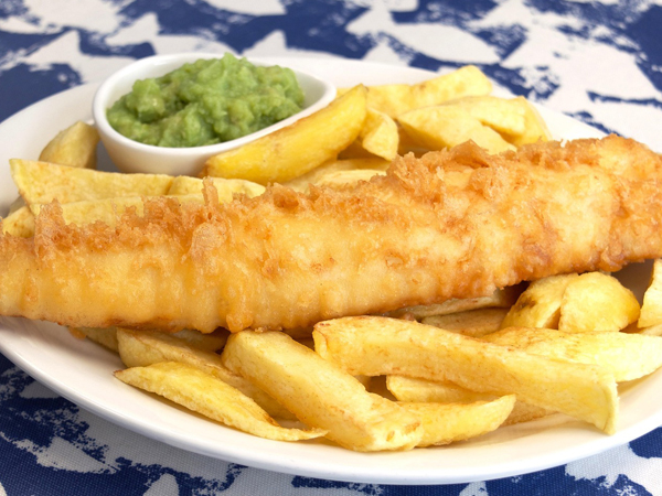 A plate of fish and chips with a side of mushy peas.