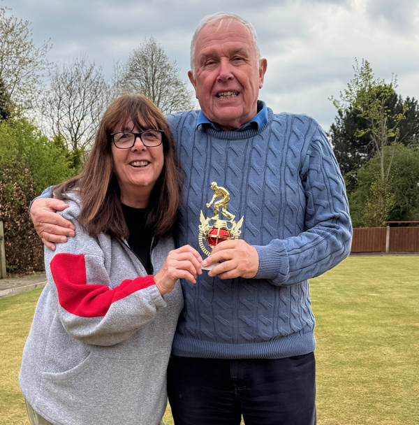 Woman and man standing on the green, posing with the small trophy.