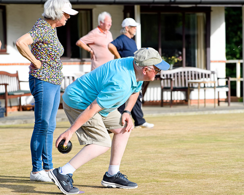 Woman and man in the foreground. The man is bending down to deliver a wood. The woman is standing behind him, watching. Two men standing in the background.