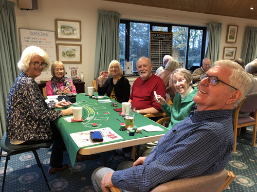 Men and women sitting at a table, playing blackjack, looking at the camera and smiling.
