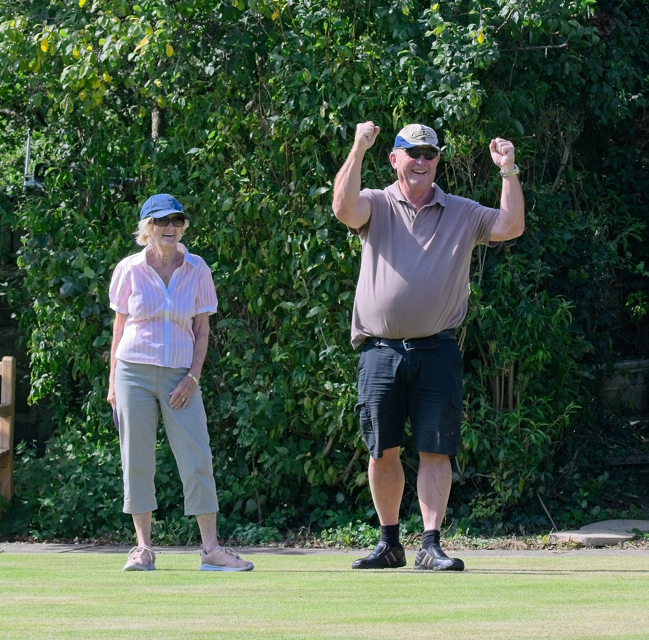 Woman and man standing on the green. The man is celebrating by raising both his arms in the air. The woman is standing off to the left behind him, smiling.