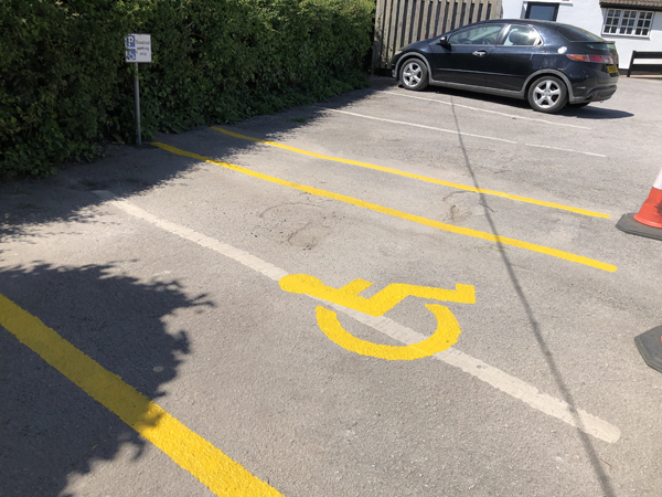 Picture of the disabled parking bay with yellow lines each side, the wheelchair icon in the middle and lines ready for diagonals on the right hand side.