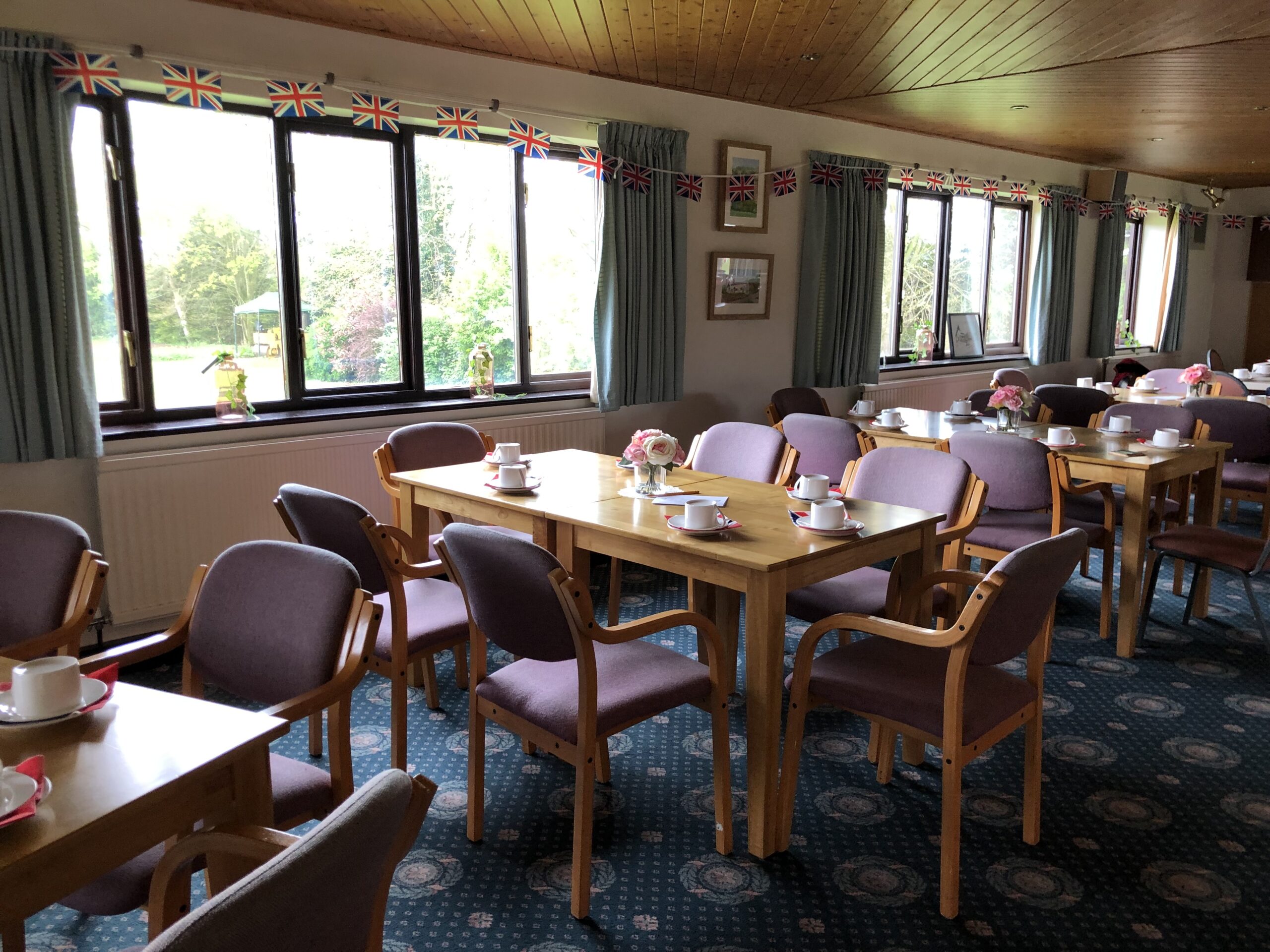 Tables and chairs in the Clubhouse set for Afternoon Tea with cups and saucers and centrepieces.
