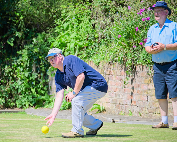 Two men on the green. One has just bowled the jack, the other is standing behind him watching