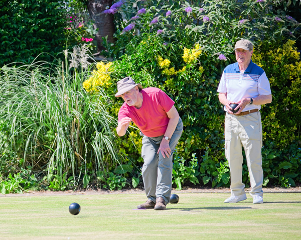 Two men on the green. The one in front has just delivered a bowl. The one behind is standing watching, waiting to bowl.