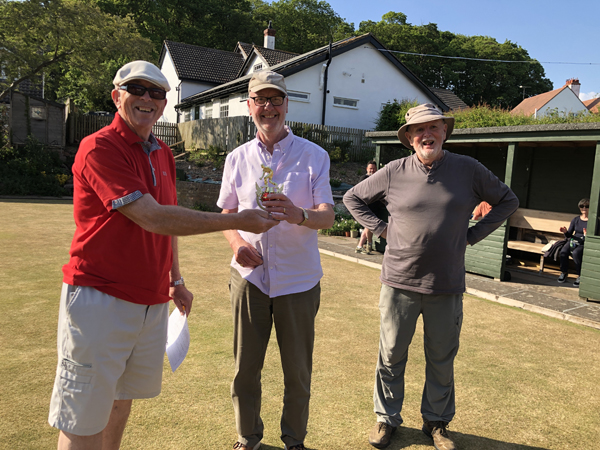 Three men standing on the green, posing with the small trophy