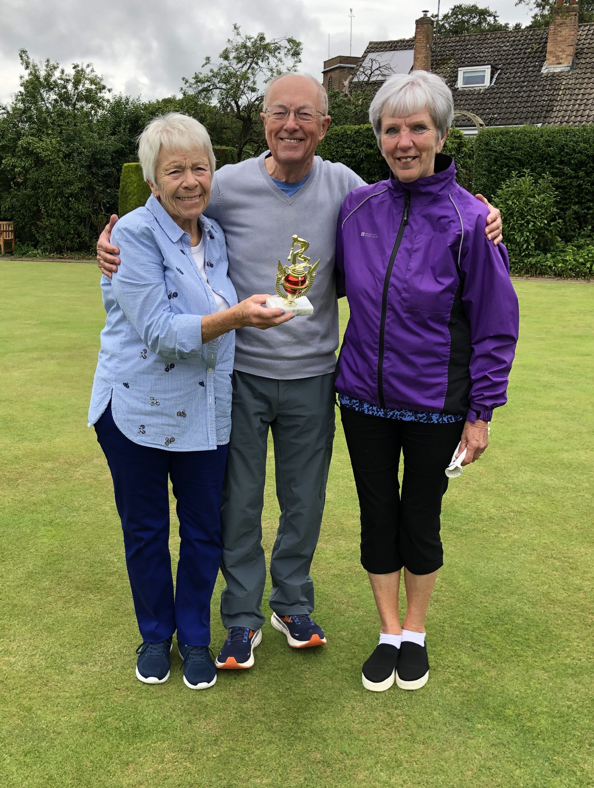 Two women and a man posing on the green with the small trophy.
