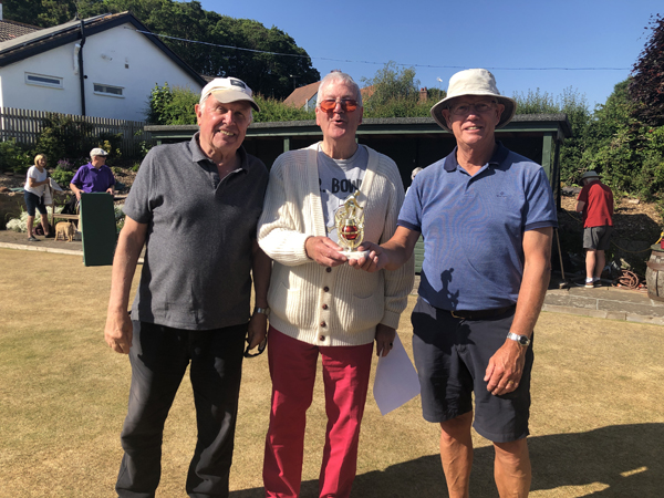 Three men standing on the green, posing with the small trophy