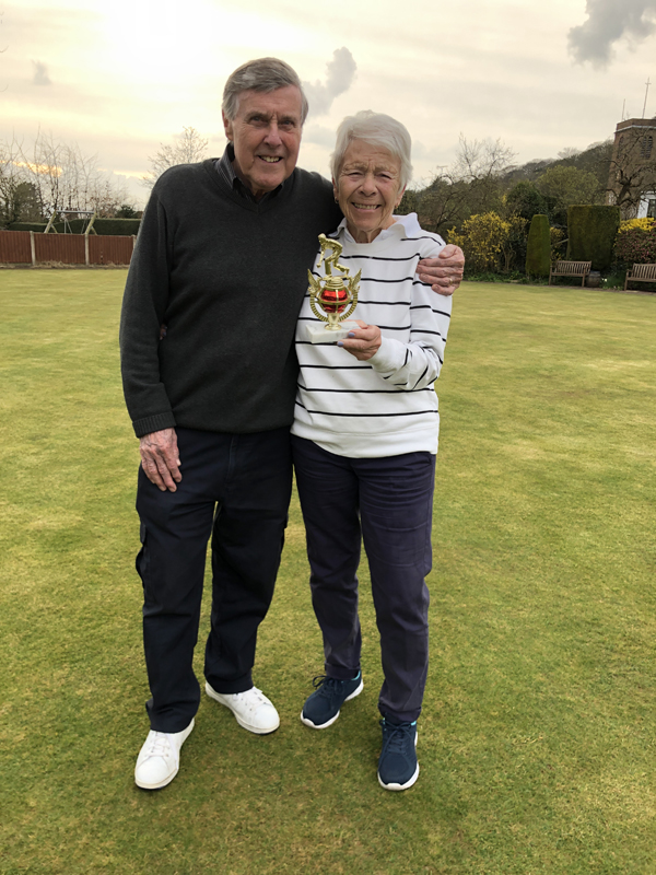 A man and a woman standing on the green, posing with the small trophy.