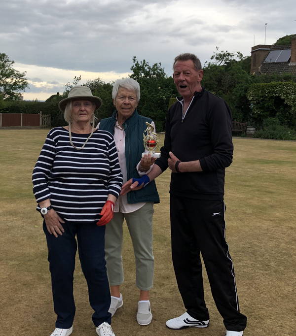 Two women and a man posing on the green with the small trophy.