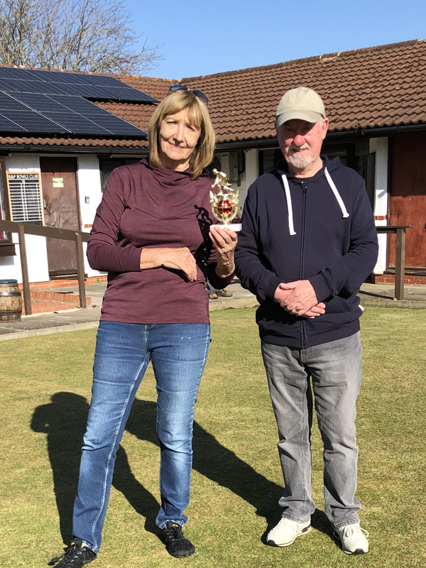 A woman and a man standing on the green, posing with the small trophy.