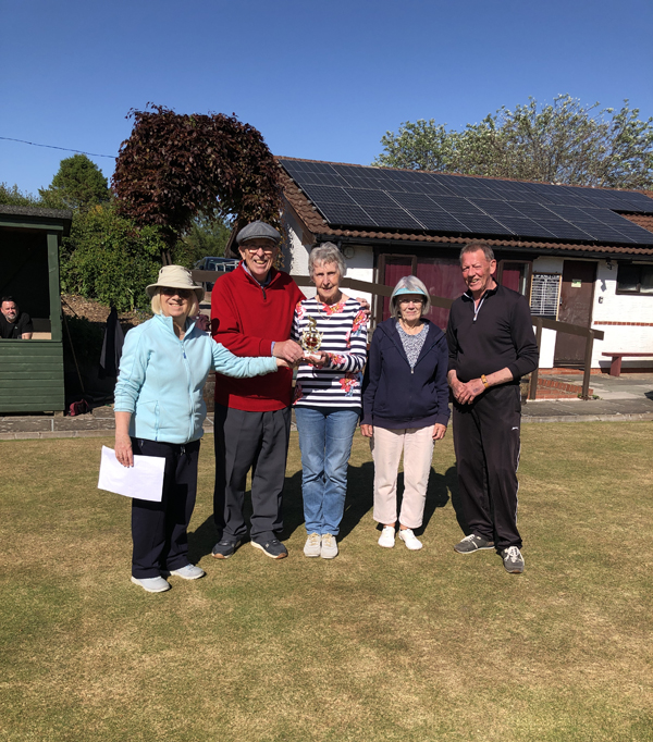 Three women and two men standing on the green, posing with the small trophy