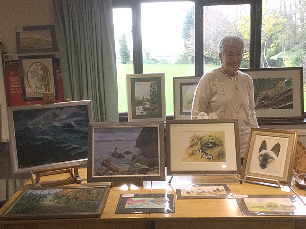 Pat standing behind a table displaying her paintings.