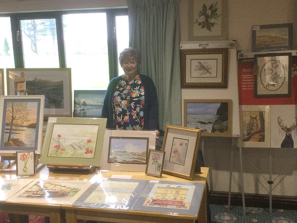 Wendy standing behind a table, displaying her paintings.