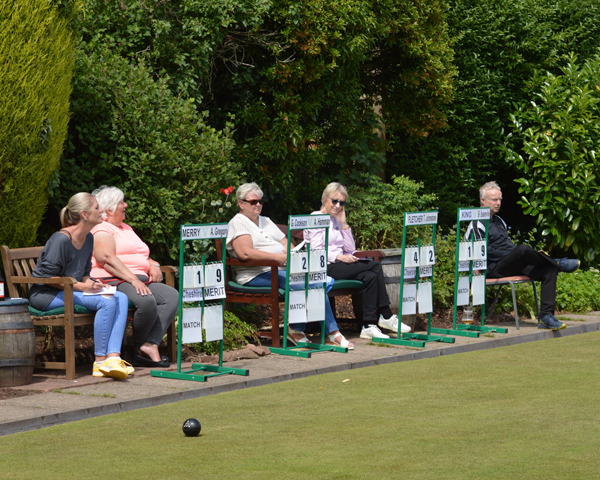 Four scoreboards at the end of the green. Four women and one man sitting behind them.