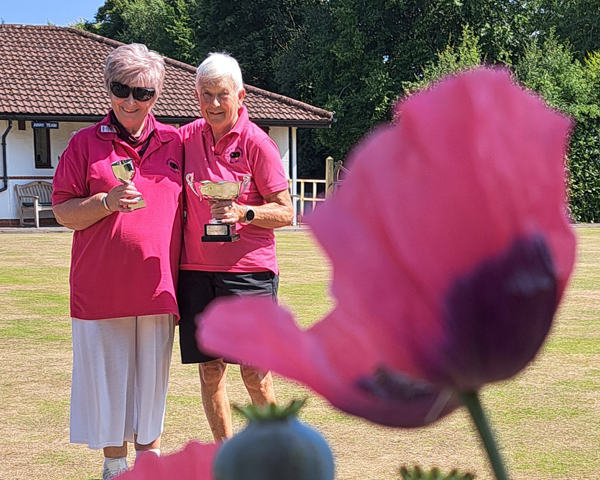 Wendy and Angela on the green holding their trophies. In the foreground a large red poppy.