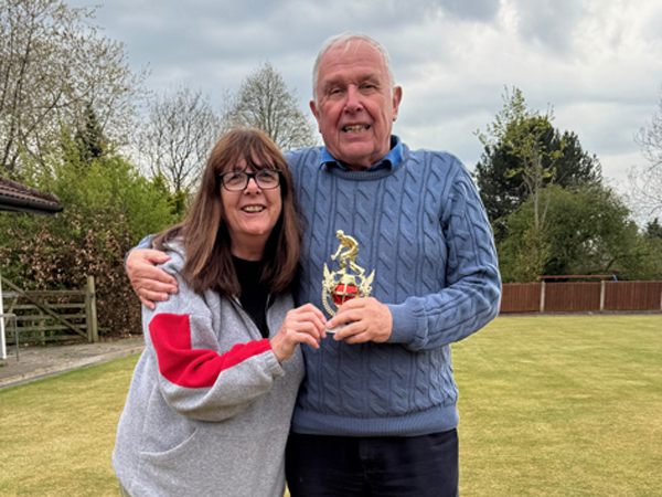 Woman and man standing on the green, posing with the small trophy.