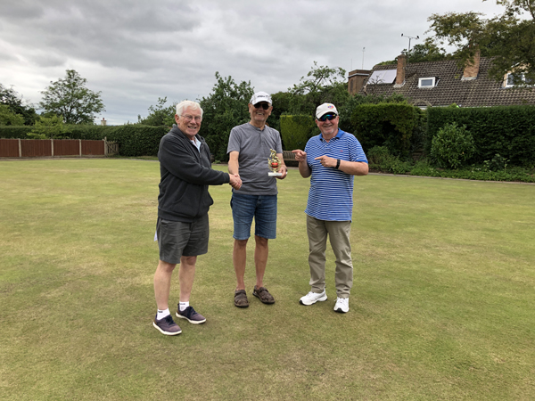 Three men standing on the green, posing with the small trophy.