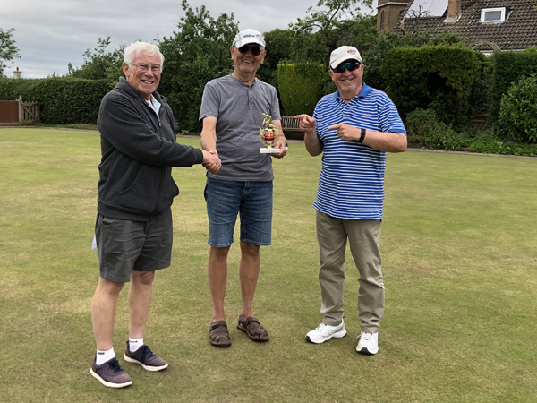 Three men standing on the green, posing with the small trophy.