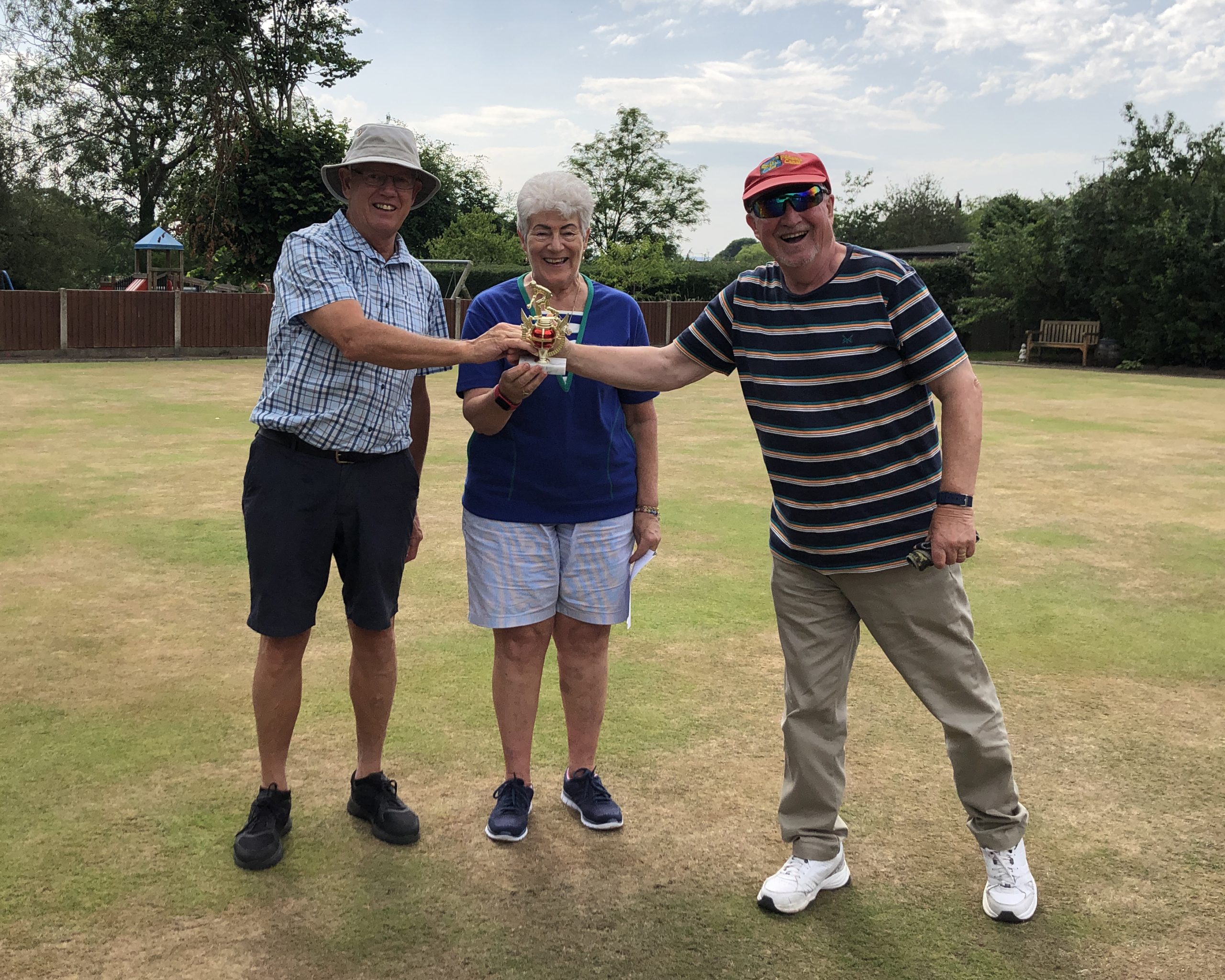 Two men standing either side of a woman, posing with the small trophy.