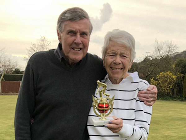 Man and woman standing on the green, posing with the small trophy.