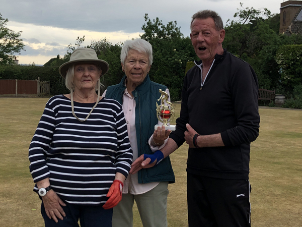 Two women and a man posing on the green with the small trophy.