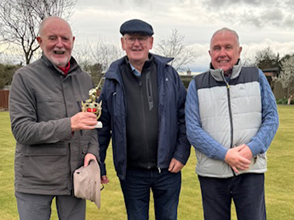 Three men standing on the green, posing with the small trophy.