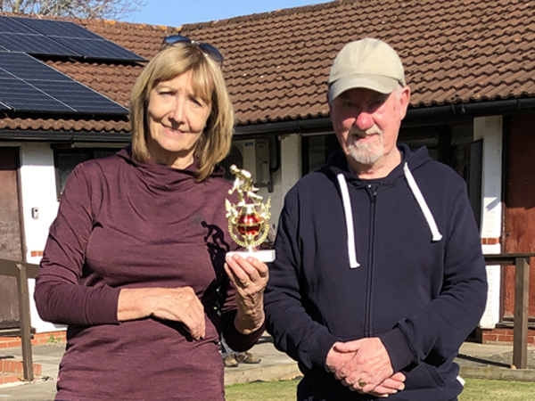 Woman and man standing on the green, posing with the small trophy.
