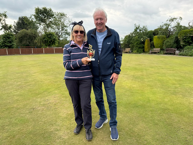 Woman and man standing on the green posing with the small trophy.