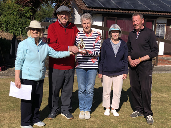 Three women and two men standing on the green, posing with the small trophy