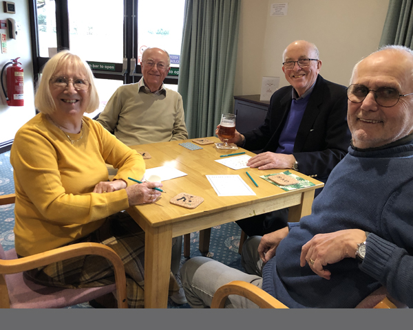 Three men and one woman sitting at a table at a Beetle Drive. All turned to the camera and smiling.