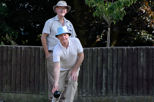 Man bowling. He has just delivered the bowl. A second man is standing behind him, watching.