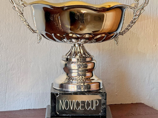 A trophy on a marble effect plinth. It is a cup with ornate handles. The plaque on the plinth reads Novice Cup.