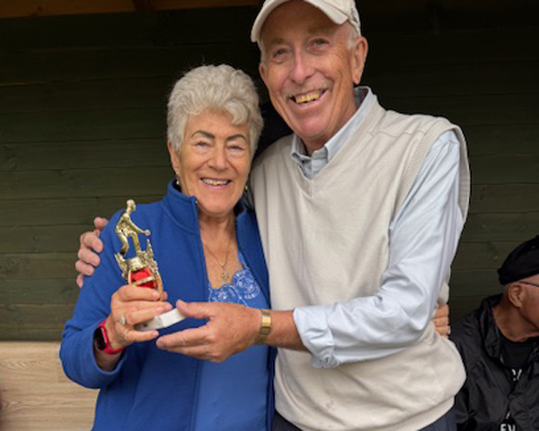 A woman and a man standing in the cover of the Bowls shelter. They are posing with the small trophy.