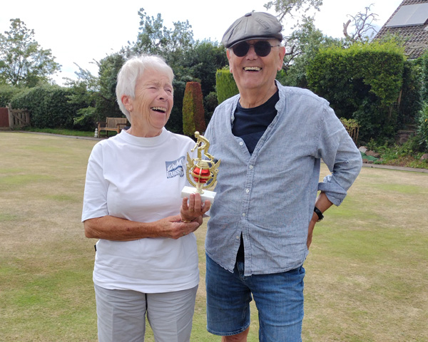 Woman and man on the green, posing with the trophy and laughing