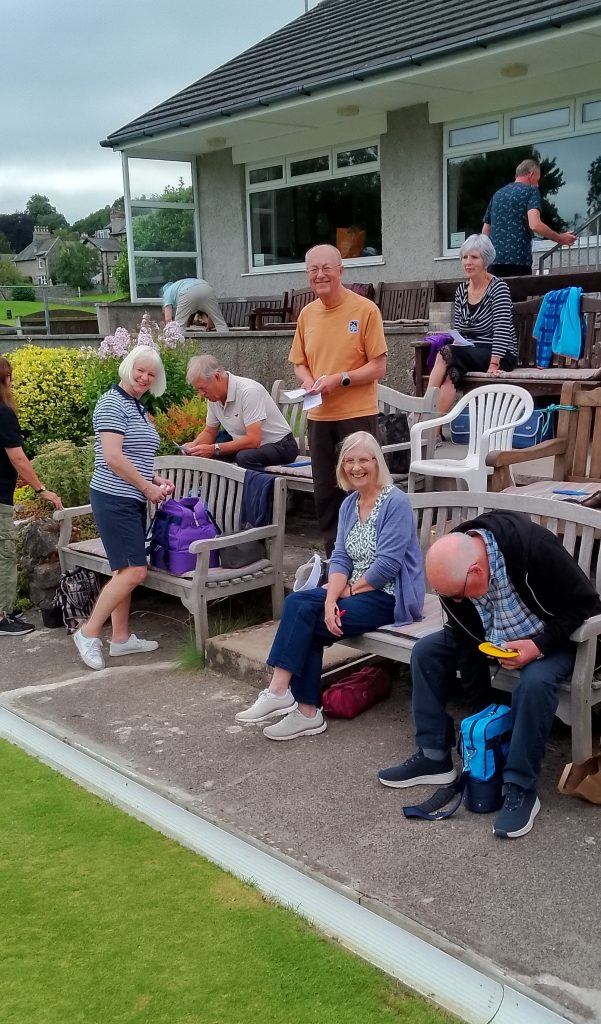 A group of bowlers sitting and standing on tiers at Arnside Bowling Club.
