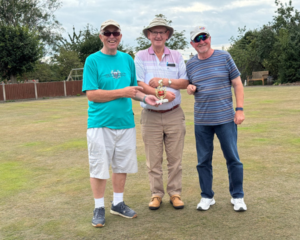 Three men standing on the green, posing with the small trophy.