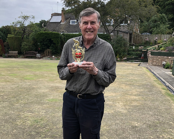Man standing on the green holding the small trophy.