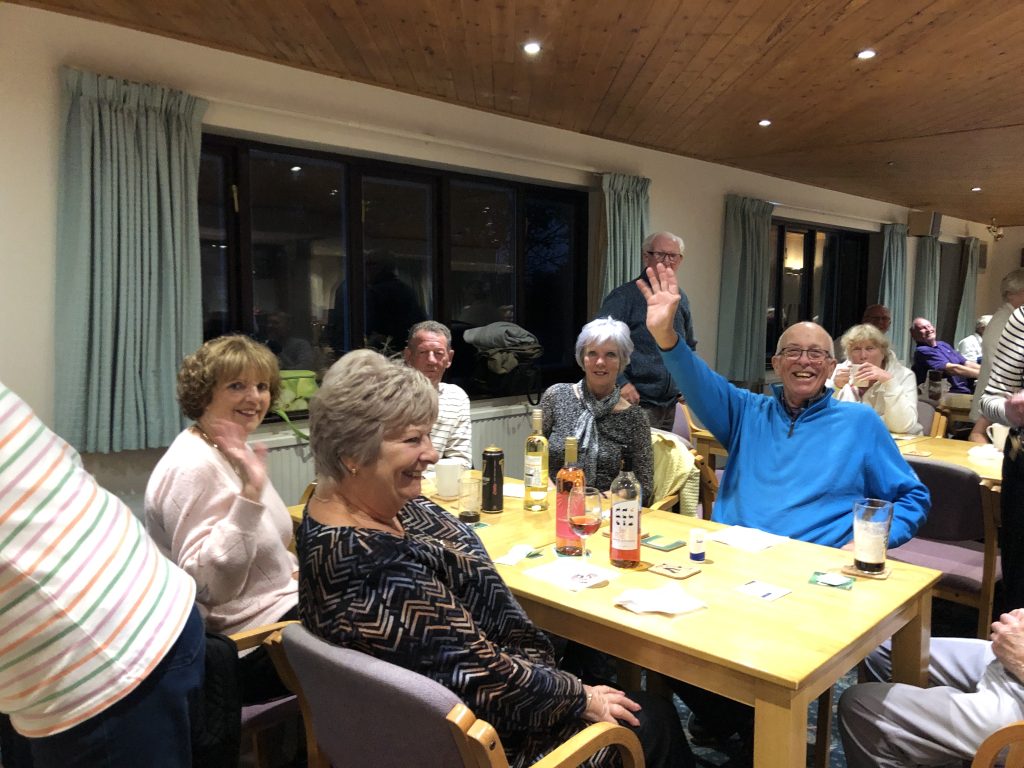 Wendy, Jackie, Roy, Margaret, Alan sitting at a table with drinks, smiling at the camera. Alan is waving. Behind you can see Brian and Heather.