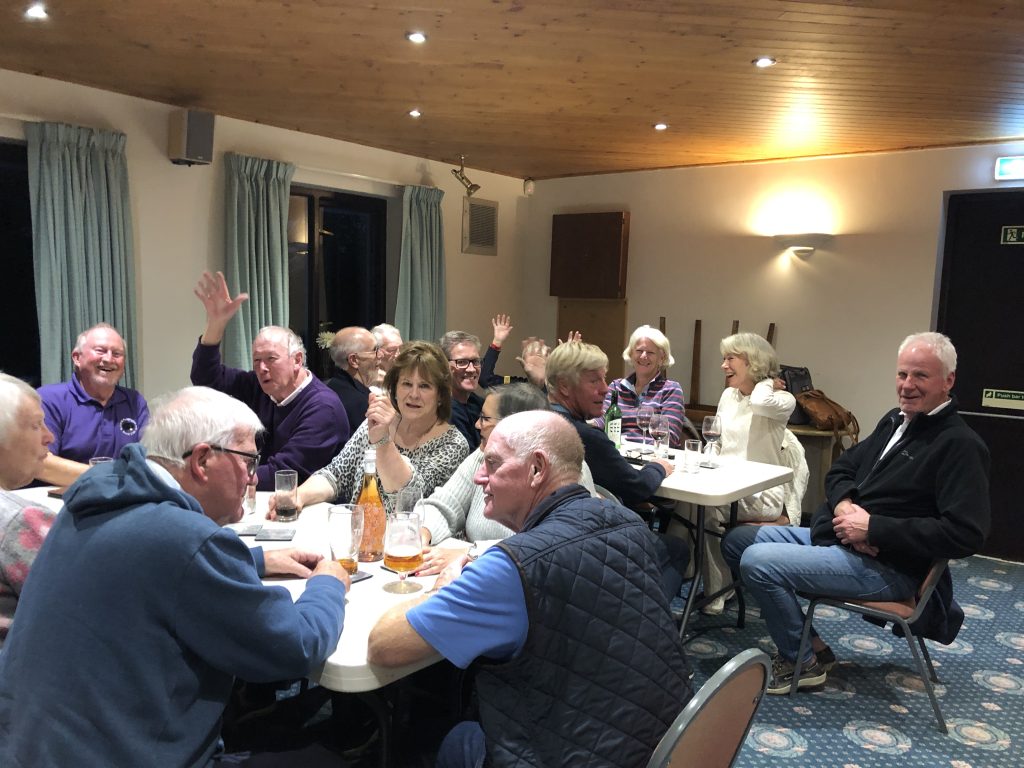 People sitting at tables, smiling and waving. Pat, Maggie, Ian N, Ralph, Viv, Pat P, Charlie, Dave T, Jon, Howard, Lindy, Lindy's guests.