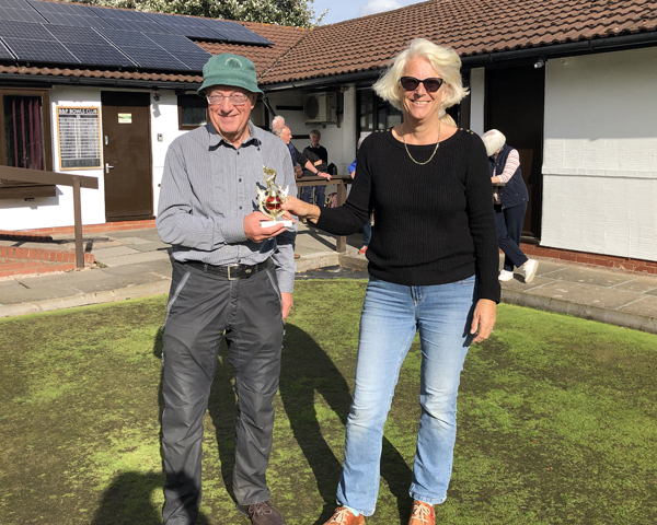 Man and woman standing on the green holding the trophy.