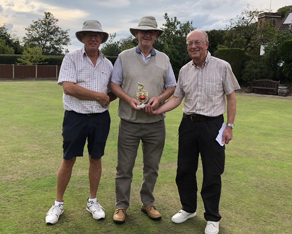 Three men standing on the green, The middle man is holding the small trophy.