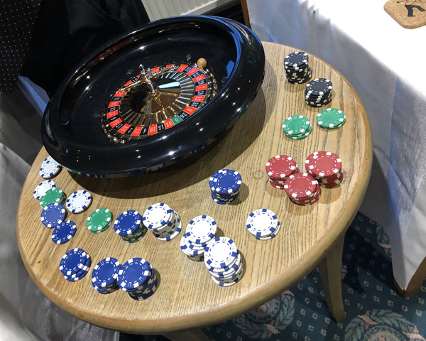 A round table with a roulette wheel and piles of chips (blue, white, green, red).