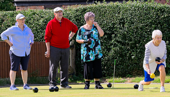 Three women and one man on the green in a line. The woman on the right is just about to deliver the jack.