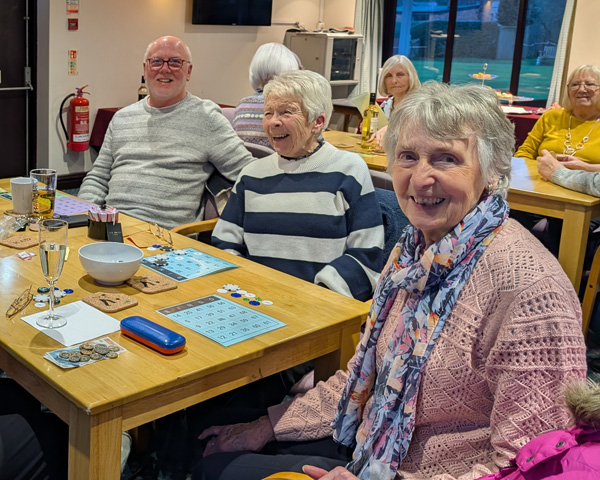 Two women and a man sitting at the table with bingo cards, laughing.