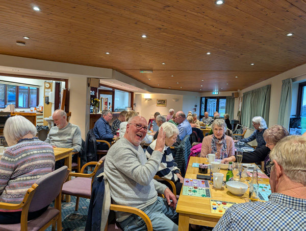 People sitting at a table playing bingo. One man waving at the camera.