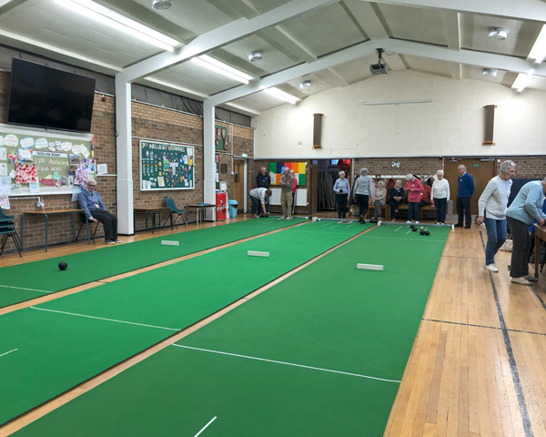 View of three mats in Claremount Church Hall with bowlers around the outside.