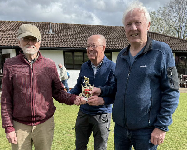 Three men standing on the green holding the trophy.