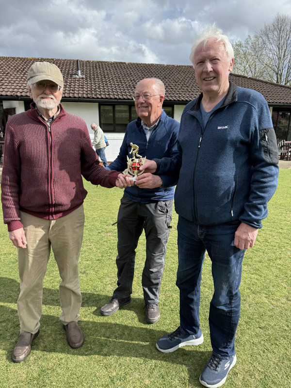 Three men standing on the green holding the trophy.