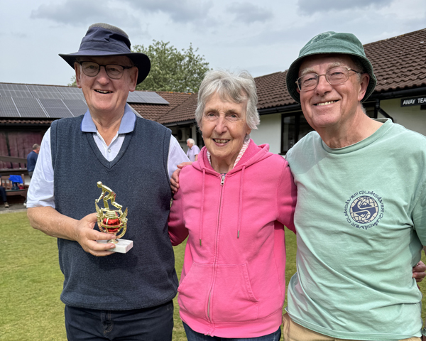 Woman standing between two men. The man on the left is holding the small trophy.